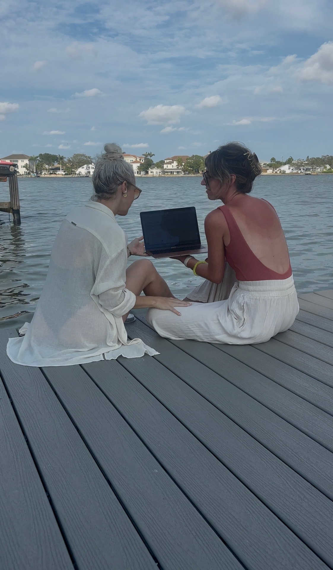 Kasey Ryan reviewing work on a laptop with a colleague while sitting on a dock by the water